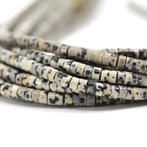 May include: A strand of light brown and black dalmatian jasper beads. The beads are small and round, and they are strung together on a clear thread.