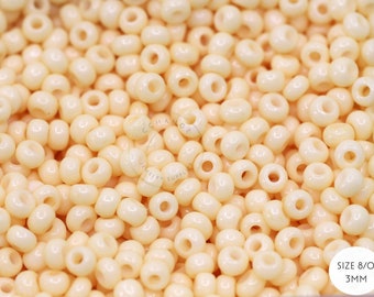 May include: A close-up of a pile of small, white, round seed beads. The beads are 8/0 size and 3mm in diameter.