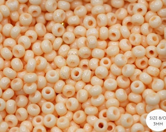 May include: A close-up shot of a pile of small, round, off-white beads. The beads have a hole through the center and are approximately 3mm in diameter. The text "SIZE 8/0 3MM" is in a white circle in the bottom right corner.