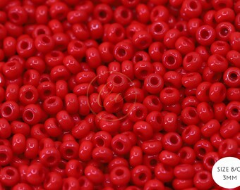 May include: A close-up image of a pile of small, red, round seed beads. The beads are 3mm in size and are commonly used for jewellery making.