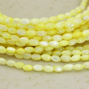 Può includere: Una collana di perline ovali di conchiglia gialla. Le perline hanno una finitura madreperlacea e sono infilate su un filo trasparente.