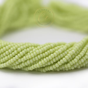 May include: A strand of light green seed beads. The beads are small and round, and they are arranged in a loose, flowing pattern.
