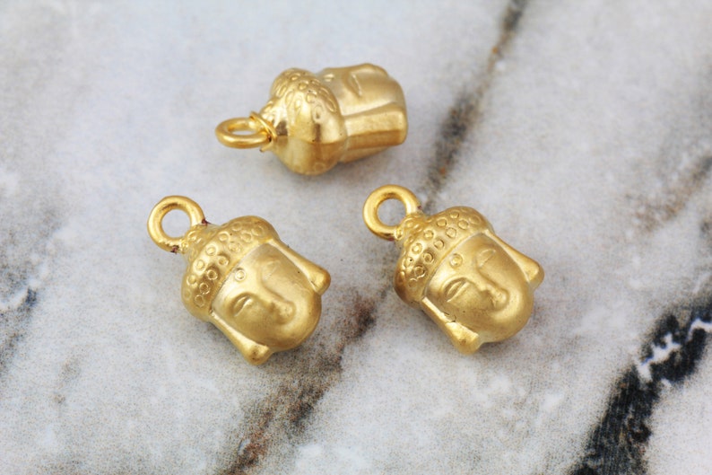 May include: Three gold-colored metal charms featuring the face of Buddha. Each charm has a loop for attaching to a necklace or bracelet.