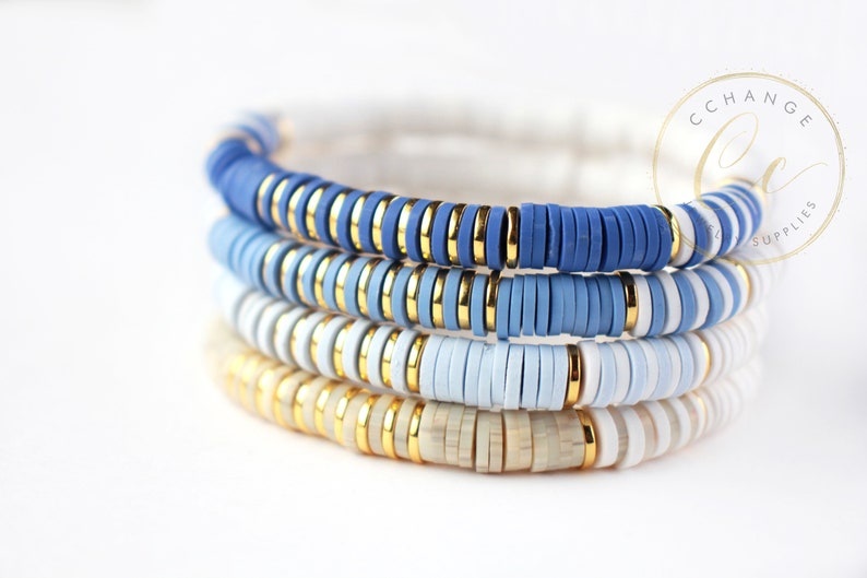 May include: Four stacked bracelets with blue, white, and gold beads. The bracelets are made of ceramic and have a layered ombre effect.