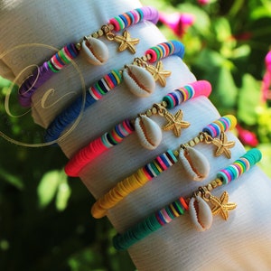 May include: A collection of colorful disc bracelets. Each bracelet features a different solid color, accented with rainbow stripes. Gold starfish and seashell charms dangle from each bracelet, creating a beachy aesthetic. The bracelets are displayed on a white surface.