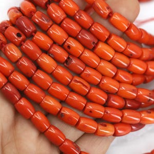 May include: Strands of vibrant orange-red coral beads. The beads are barrel-shaped and strung together, showcasing a natural, organic texture. The coral's color varies slightly, adding depth to the design. Ideal for jewelry making.
