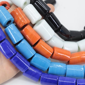 May include: Strands of colorful, cylindrical beads in shades of blue, orange, white, and black. The beads are strung together, showcasing a variety of colors and textures. These beads are suitable for jewelry making and crafting projects.