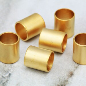 Puede incluir: Seis anillos de metal de color dorado, cada uno con un acabado liso y pulido. Los anillos est&aacute;n dispuestos en semic&iacute;rculo sobre una superficie de m&aacute;rmol blanco.