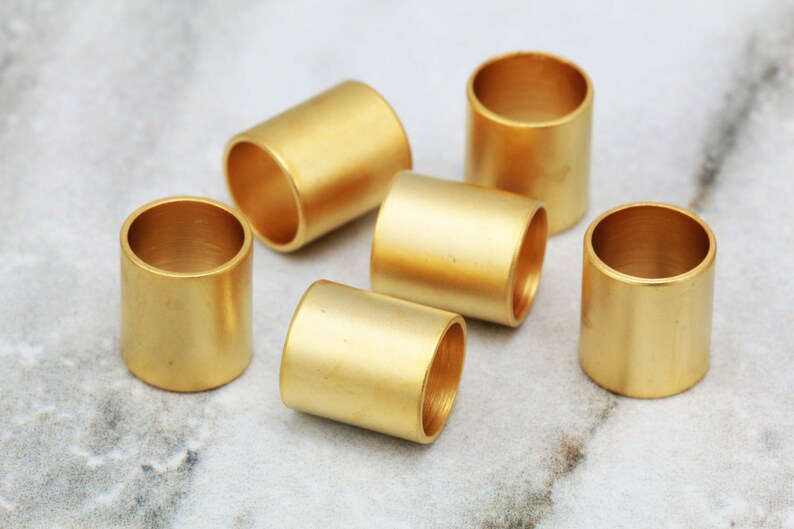 Puede incluir: Seis anillos de metal de color dorado, cada uno con un acabado liso y pulido. Los anillos est&aacute;n dispuestos en semic&iacute;rculo sobre una superficie de m&aacute;rmol blanco.