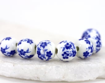 Puede incluir: Una hebra de cuentas de cerámica blanca con diseños florales azules. Las cuentas son redondas y tienen un acabado brillante.