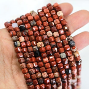 Puede incluir: Una hebra de cuentas de piedras preciosas rojas, marrones y negras. Las cuentas son de forma cuadrada y tienen un acabado facetado.