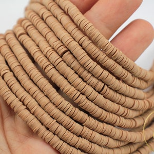 May include: Tan-colored, flat disc beads, likely polymer clay, are shown in a close-up shot. The beads are strung together, creating a flowing, textured appearance. These beads are ideal for jewelry making and crafting.