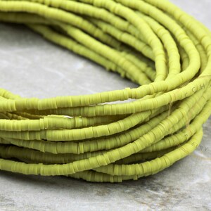 May include: Close-up of a pile of light green, flat, disc-shaped beads. The beads are stacked in a loose, organic arrangement, creating a textured surface. These beads are ideal for jewelry making and other craft projects.