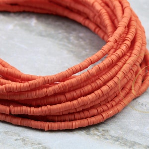 May include: Close-up of a pile of coral-colored, flat, round beads. The beads are strung together, creating a layered effect. The beads are uniform in size and shape, and the color is consistent throughout.