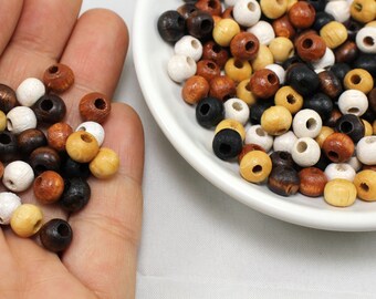 May include: A close-up of a hand holding a variety of wooden beads in brown, black, white, and natural wood tones. The beads are round and have a hole in the center. The beads are also shown in a small white bowl.