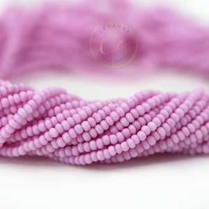 May include: A close-up of a strand of light pink seed beads. The beads are small and round, and they are arranged in a tight, even pattern.