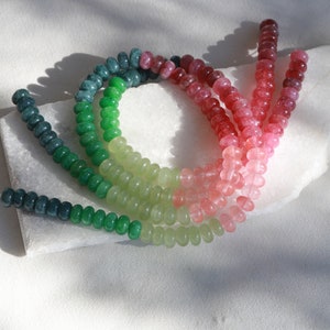 May include: A set of green, light green, and pink gemstone beads. The beads are round and have a smooth, polished finish. They are arranged in a rainbow pattern.