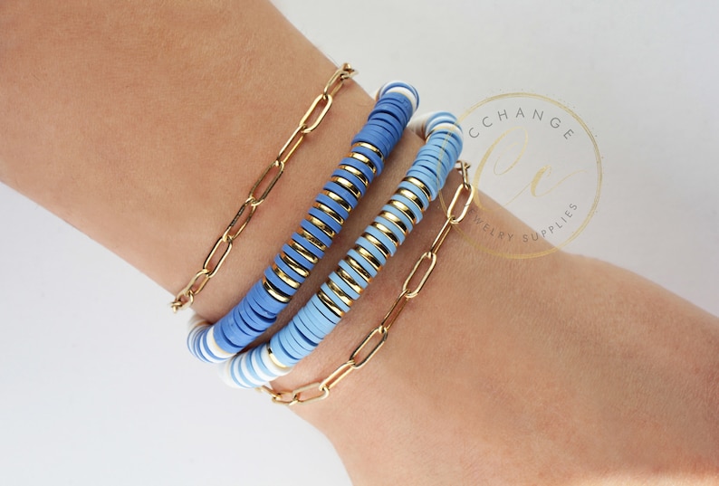 May include: A set of three bracelets featuring blue and white beads with gold accents. The bracelets are stacked on a person's wrist.