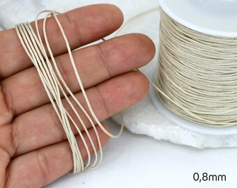 May include: A spool of 0.8mm thick, off-white elastic cord. The cord is wound around a white plastic spool. The cord is shown in a hand, demonstrating its thickness.
