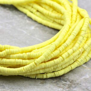 May include: A close-up of a strand of bright yellow polymer clay beads. The beads are small and round, and they are strung together in a long strand. The beads are arranged in a loose, flowing pattern.