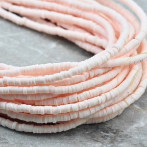 May include: A strand of pale pink round ceramic beads. The beads are small and have a slightly irregular shape. The beads are strung on a clear thread.