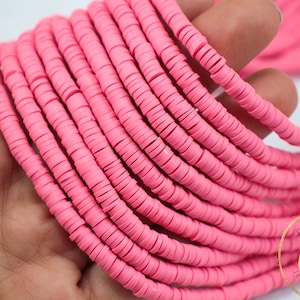 May include: A strand of pink polymer clay beads, each bead is a flat circle with a hole in the center. The beads are stacked on top of each other, creating a thick, colorful strand.