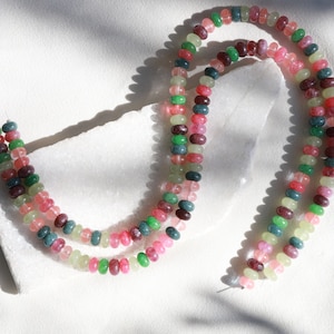 May include: A strand of multi-colored beads made of jade. The beads are pink, green, and light green. The beads are strung on a clear string.