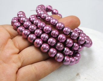 Op de afbeelding: Een streng ronde, metallic roze kralen. De kralen hebben een glanzende, reflecterende afwerking.