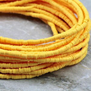 May include: A close-up of a spool of yellow polymer clay beads. The beads are small and round, and they are arranged in a coil.