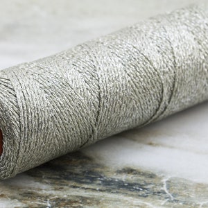 May include: A spool of silver metallic thread with a red plastic center.