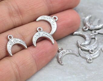 May include: A close-up of silver crescent moon charms with intricate designs. The charms have a loop at the top for attaching to jewelry or other crafts.
