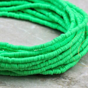 May include: A strand of bright green polymer clay beads. The beads are small and round, and they are strung together in a long strand. The strand is coiled up on a white surface.