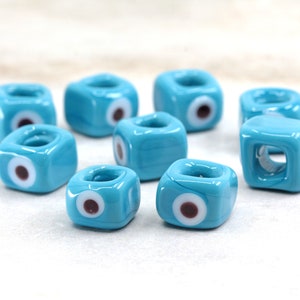 May include: Eight turquoise blue glass beads with a white evil eye charm. Each bead has a hole in the center for stringing.