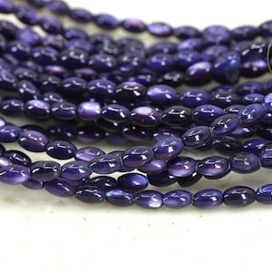 Può includere: Una collana di perline ovali di colore viola. Le perline hanno una finitura madreperlacea e sono infilate su un filo trasparente.