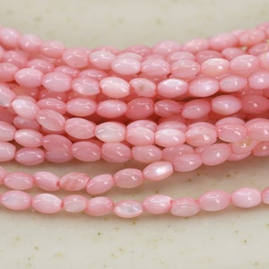 Può includere: Un filo di perline ovali di conchiglia rosa. Le perline hanno una lucentezza madreperlacea e sono infilate su un filo trasparente.