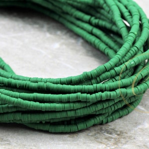 May include: Close-up of a pile of green, flat, disc-shaped beads. The beads are stacked in multiple strands, creating a textured, layered effect. The beads are a solid, matte green color, and appear to be made of plastic or a similar material. Ideal for jewelry making.