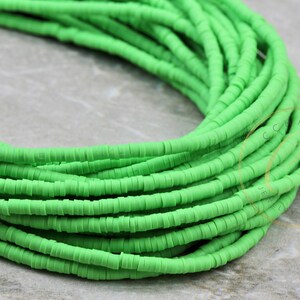 May include: A close-up of a strand of bright green polymer clay beads. The beads are small and round, and they are arranged in a coil.
