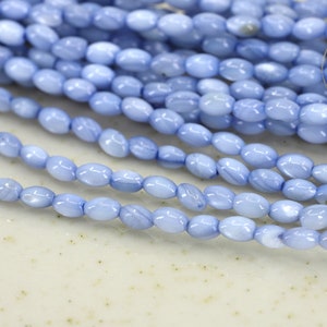 Può includere: Una collana di perline ovali di colore azzurro chiaro. Le perline sono realizzate in un materiale liscio e lucido e hanno una finitura leggermente iridescente.