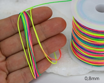 Op de afbeelding: Een spoel neonkleurig gewaxt koord, 0,8 mm dik, met een hand die een paar strengen van het koord vasthoudt.