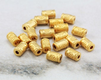 Könnte beinhalten: Ein Haufen goldfarbener Metallperlen mit einem strukturierten Design. Die Perlen sind zylindrisch und haben ein Loch in der Mitte.