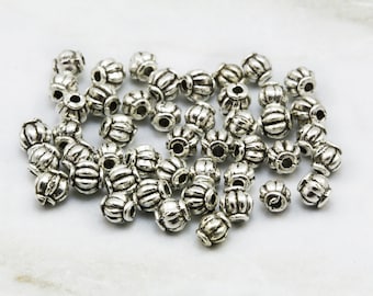 Puede incluir: Un montón de cuentas de metal plateado con un diseño decorativo. Las cuentas son redondas y tienen un patrón en relieve.