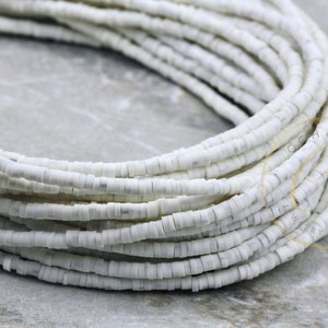 May include: A close-up of a white ceramic bead strand. The beads are small and round, and they are arranged in a tight coil. The beads are smooth and shiny, and they have a slight iridescent sheen.