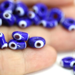 Puede incluir: Primer plano de una colección de cuentas azules y blancas de ojo turco. Las cuentas son de varias formas y tamaños, y algunas están enhebradas en una cuerda.