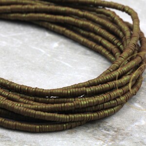 May include: A strand of dark green metallic beads, each bead is a flat, thin circle. The beads are arranged in a coil shape.