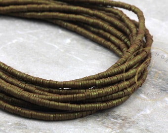 May include: A strand of dark green metallic beads, each bead is a flat, thin circle. The beads are arranged in a coil shape.