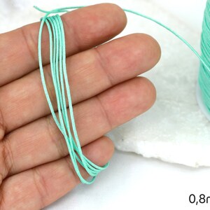 May include: A spool of light green elastic cord, 0.8mm thick, held in a hand. The cord is smooth and appears to be made of nylon.