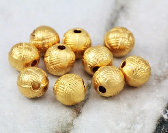 May include: A group of ten gold-colored metal beads with a woven pattern. The beads have a hole through the center for stringing.