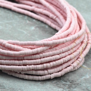 May include: A close-up of a strand of pink ceramic beads. The beads are small and round, and they are arranged in a coil.