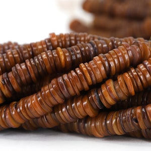 May include: A strand of brown and tan shell beads, each bead is a flat disc with a slightly raised center. The beads are stacked on top of each other, creating a textured look.