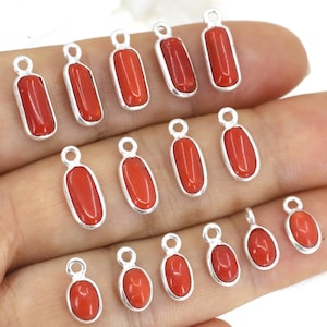 Può includere: Una collezione di ciondoli in corallo rosso con montature in metallo color argento. I ciondoli sono di varie forme, tra cui rettangolari e ovali, e hanno un piccolo anello nella parte superiore per il fissaggio a una catena o ad altro componente di gioielleria.